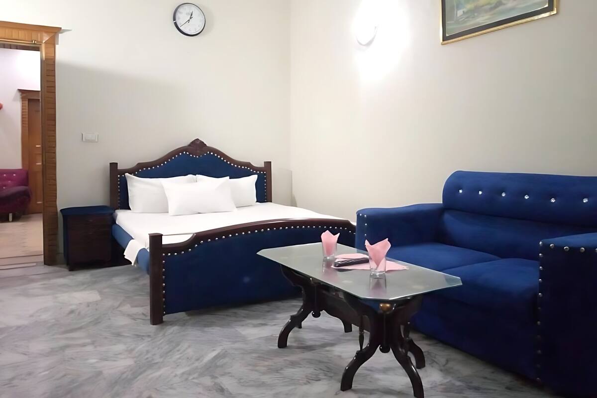 Un dormitorio con cama, un sofá azul, una mesita, un reloj y un cuadro en la pared.