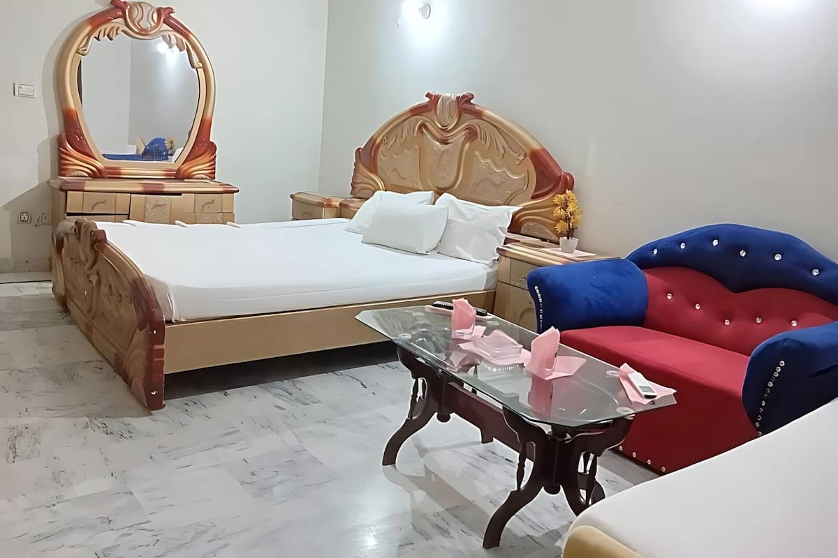 Un dormitorio con cama, mesita de noche, cómoda, espejo, mesa de centro de vidrio y sofá rojo y azul.