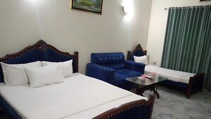Una camera d'albergo con un letto, una poltrona blu, un tavolino e una tenda verde.