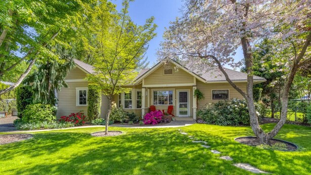 A single-story house with a front porch, surrounded by a well-maintained lawn and flowering plants. - Rosé  All Day Hideaway (Walla Walla)