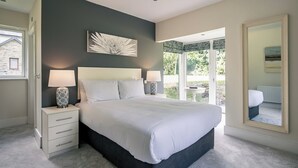 Une chambre à coucher avec un grand lit, deux tables de chevet avec des lampes, une œuvre d’art accrochée au mur et un grand miroir.