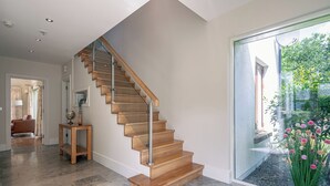 Un escalier moderne avec des marches en bois et des rampes en métal, menant à une pièce dotée d’une grande porte vitrée et offrant une vue sur la verdure environnante.