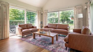 Un salon spacieux avec deux canapés, une table basse et une vue sur un jardin grâce à de grandes fenêtres.