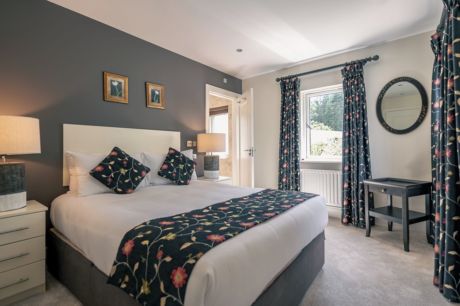 A bedroom with a bed, bedside lamps, a desk, and curtains.