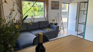 A modern living room with a grey sofa, a wooden dining table, and a bottle of wine.