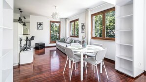 Een moderne woonkamer met een eethoek, grote ramen en uitzicht op groen.