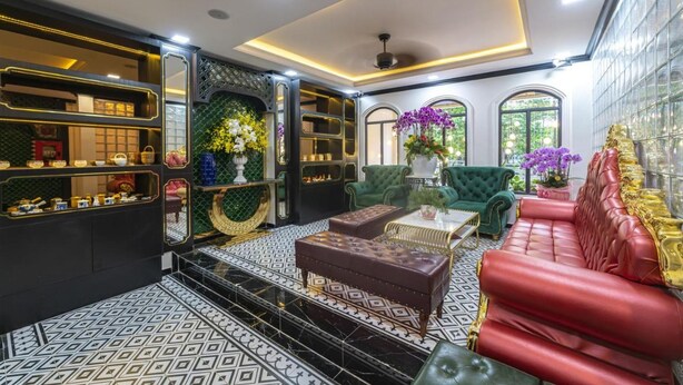 A luxurious interior with a black and white patterned floor, a red leather sofa, green armchairs, and a black and gold decorative wall. - Dancentre Airport Stays - Vyvy Hotel (Ho Chi Minh City)