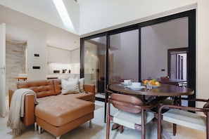 A modern living room with a leather sofa, a dining table with chairs, and a large sliding glass door leading to a balcony.