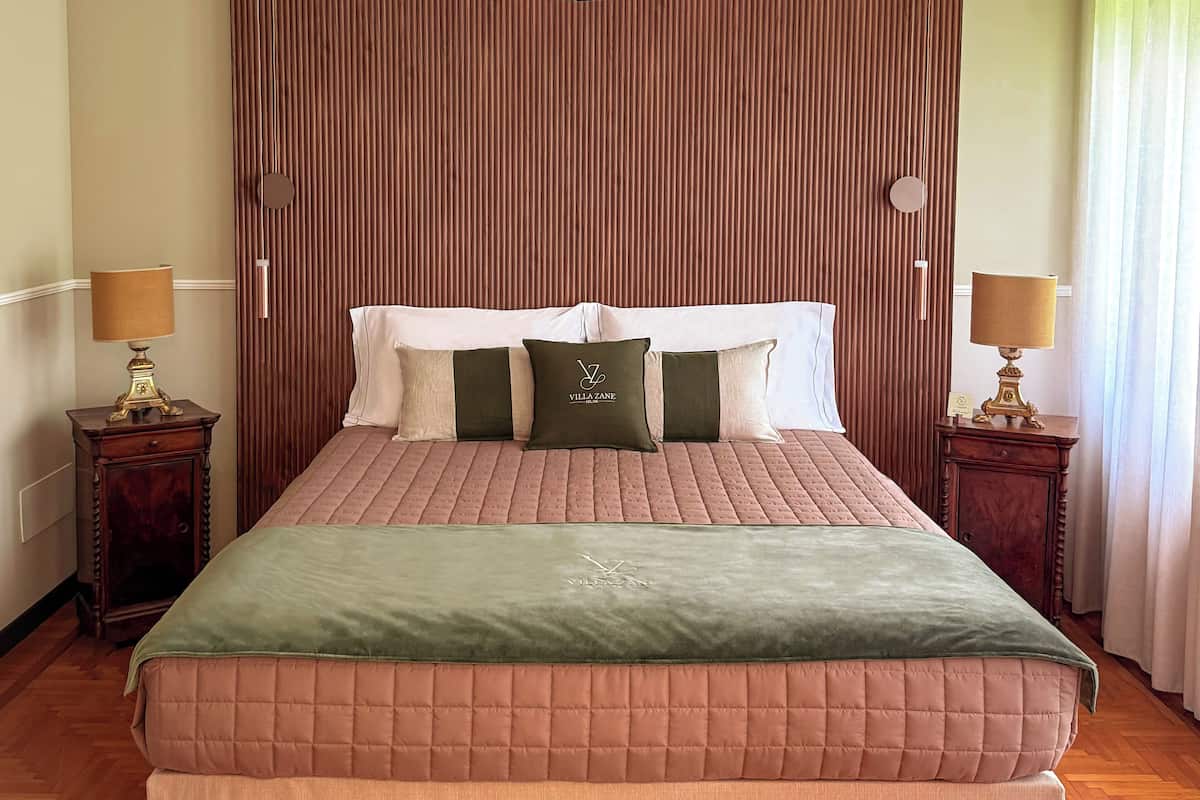 A neatly made bed with a green and pink quilted bedspread, two bedside tables with lamps, and a wooden panel wall behind the bed.