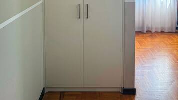A room with a large white wardrobe, wooden flooring, and a window with sheer curtains.