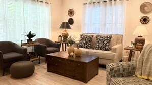 A living room with a sofa, two armchairs, a coffee table, and a patterned ottoman.
