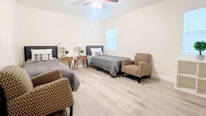 A bedroom with a bed, two bedside tables, a chair, a ceiling fan, and a window.