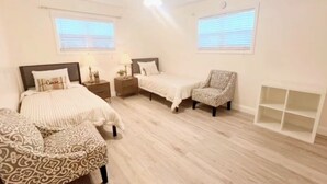 A bedroom with two beds, a chair, a nightstand, and a small shelf unit.