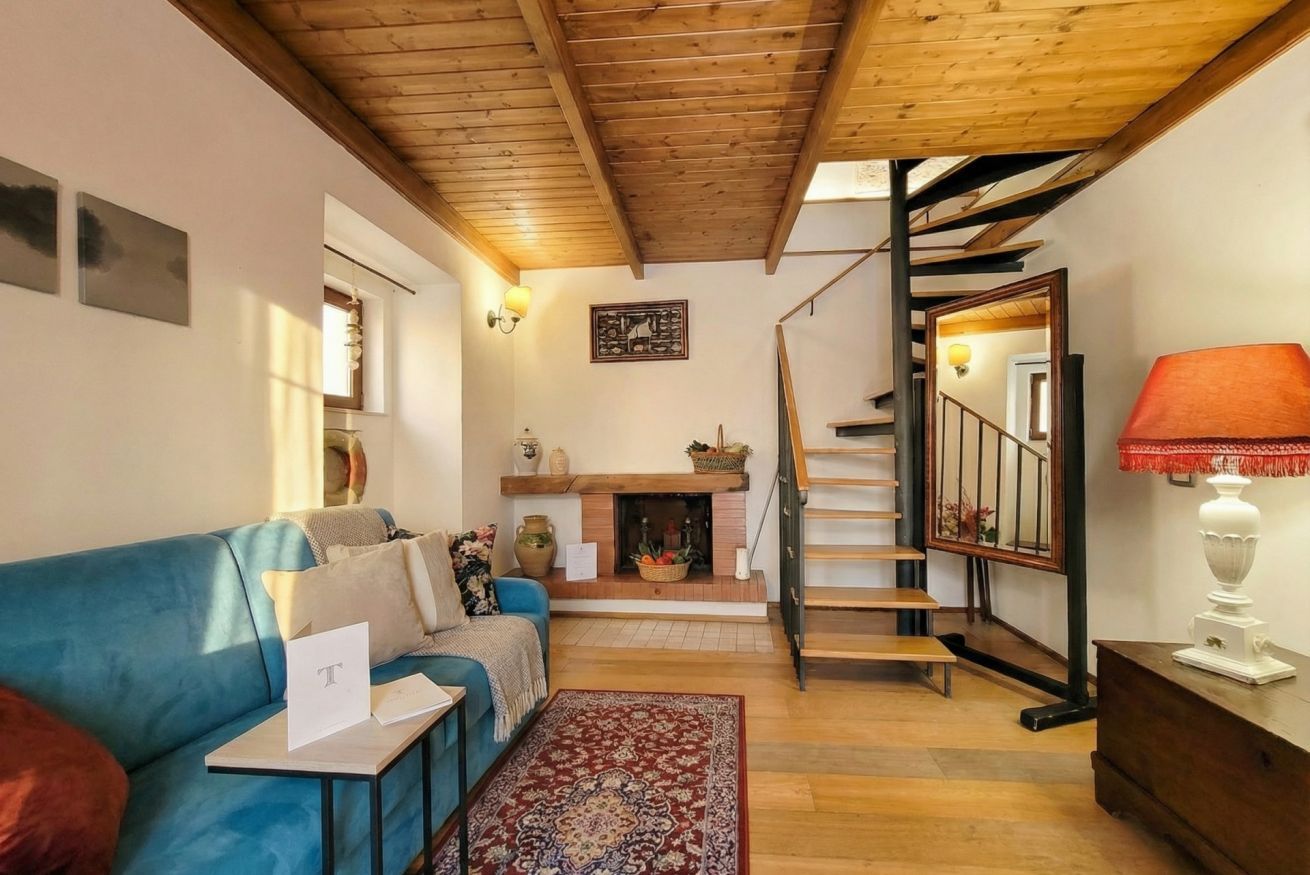 Ein gemütliches Wohnzimmer mit einem blauen Sofa, einem Kamin, einer Treppe und einer Holzbalkendecke.
