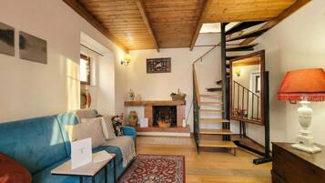 Ein gemütliches Wohnzimmer mit einem blauen Sofa, einem Kamin, einer Treppe und einer Holzbalkendecke.