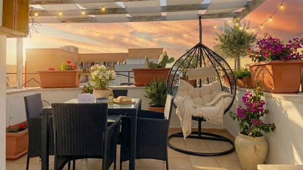 An outdoor patio with wicker furniture, a hanging chair, potted plants, and string lights. - Tatiana - Historic House (Bari)