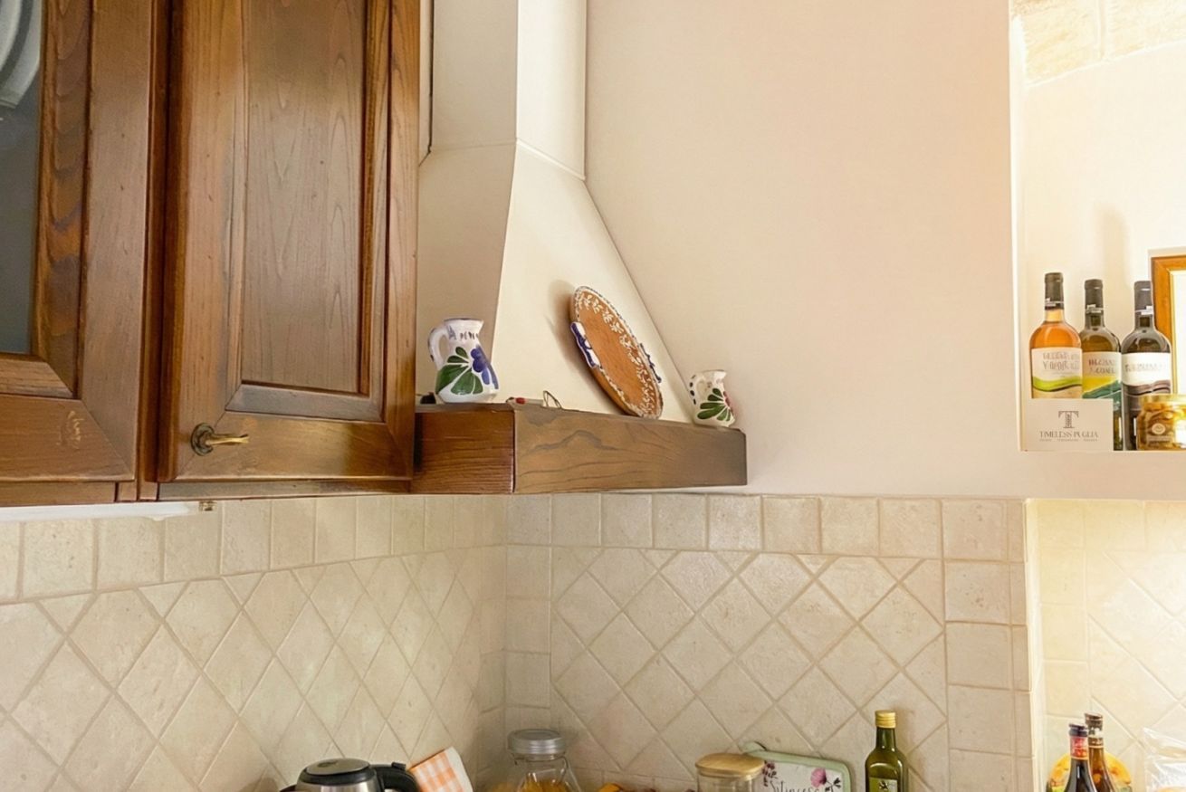 Eine Küche mit Holzschränken, einer gefliesten Spritzschutzleiste und verschiedenen Küchenutensilien, darunter ein Wasserkocher, Gläser und Flaschen.