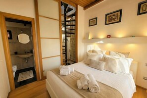 A hotel room with a bed, a bathroom with a toilet and sink, a wooden staircase, and a shelf with framed pictures. - Tatiana - Historic House (Bari)