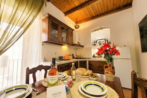 A dining area with a wooden table set for a meal, a kitchen in the background, and a vase with red flowers on the table. - Tatiana - Historic House (Bari)