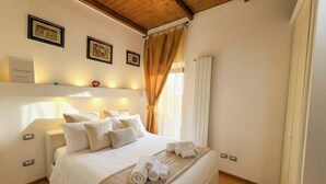 A neatly made bed with white linens and a herringbone-patterned throw, a bedside table with a lamp, and a framed picture on the wall. - Tatiana - Historic House (Bari)