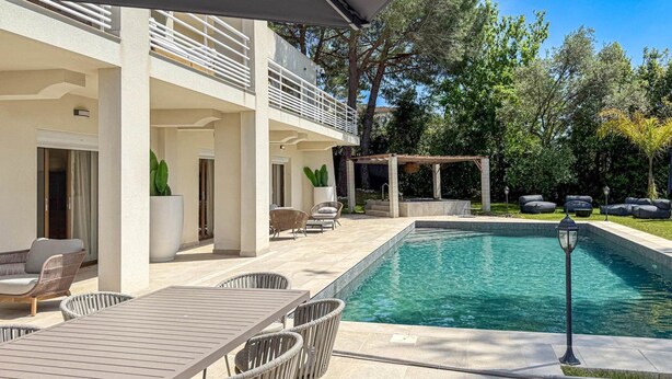 Un espace piscine extérieur moderne doté d’un patio couvert, de sièges et d’une pergola.