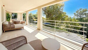 Un balcon spacieux, agrémenté de meubles en osier, d’une table ronde et offrant une vue sur les arbres et le ciel.