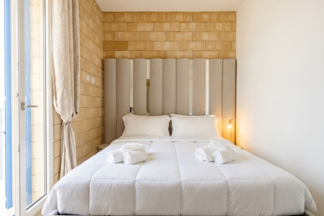 A hotel room with a brick wall, a large bed with white bedding, and a window with curtains.