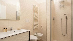 Een moderne badkamer met een wastafel, toilet, bidet en douche met glazen wanden.