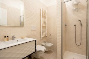 A modern bathroom with a sink, toilet, bidet, and glass-enclosed shower.