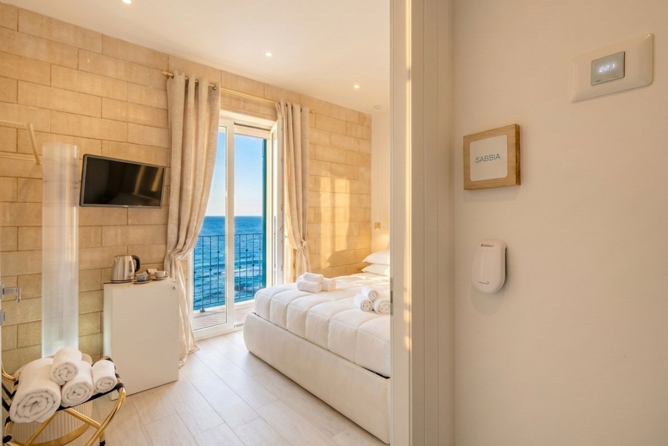 A hotel room with a bed, a TV, a small kitchenette, a balcony with a view, and a nameplate on the wall.
