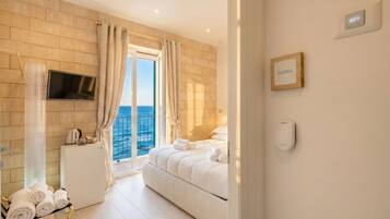 A hotel room with a bed, a TV, a small kitchenette, a balcony with a view, and a nameplate on the wall.