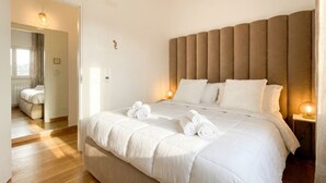 Een slaapkamer met een groot bed, een hoofdeinde, nachtlampjes en een deur naar een andere kamer.