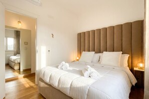 Une chambre à coucher avec un grand lit, une tête de lit, des lampes de chevet et une porte donnant sur une autre pièce.
