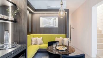 A modern living room with a sofa, a dining table, and a TV mounted on the wall.