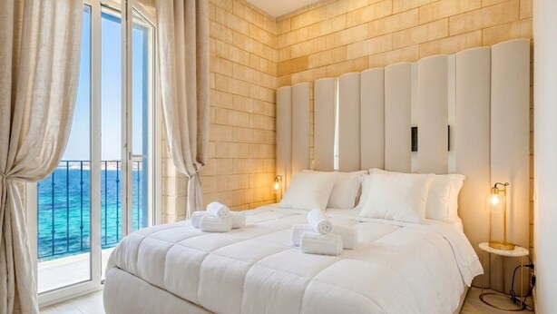 Een slaapkamer met een groot bed, een hoofdeinde, een nachtkastje en uitzicht op de oceaan.
