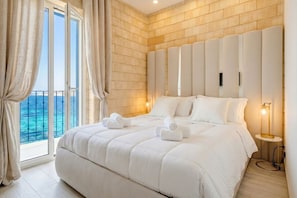 Een slaapkamer met een groot bed, een hoofdeinde, een nachtkastje en uitzicht op de oceaan.