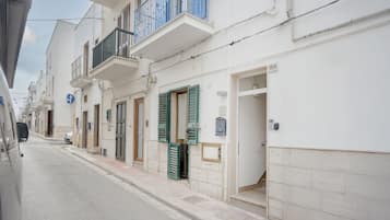 A narrow street lined with white buildings, some with balconies and shutters.