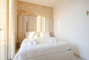 Quarto de hotel com uma cama grande, parede de tijolos e mesa de cabeceira com abajur.
