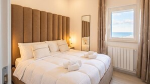 Une chambre d’hôtel avec un grand lit, une table de chevet, un miroir, une fenêtre avec des rideaux et une vue sur la mer.