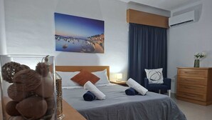 Una habitación de hotel con cama, mesita de noche, cómoda, un jarrón con flores y un cuadro en la pared.