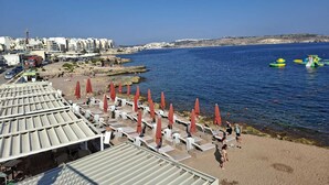 Zona de playa con tumbonas y sombrillas, vista despejada del mar y edificios al fondo.