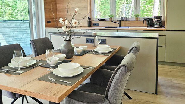 Cozinha moderna com mesa de jantar de madeira para quatro pessoas, um vaso com flores e vista para o verde lá fora.