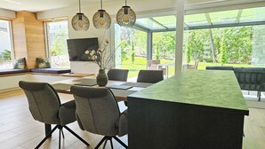 Uma sala de jantar moderna com uma mesa grande, cadeiras estofadas cinzentas e um vaso com galhos.