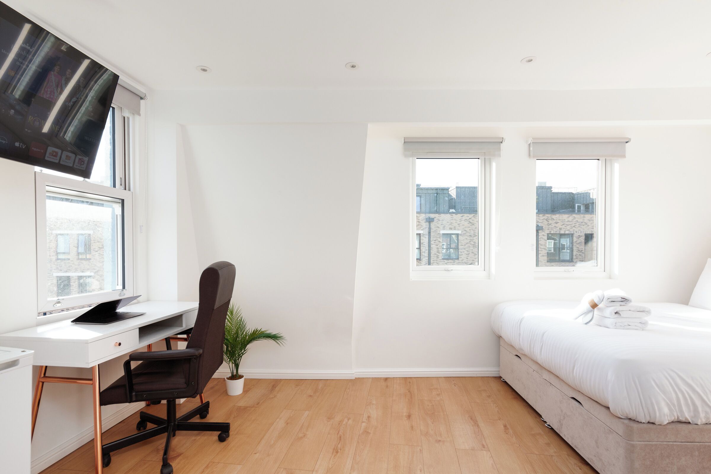 A modern bedroom with a white desk, black office chair, and a bed with white bedding.