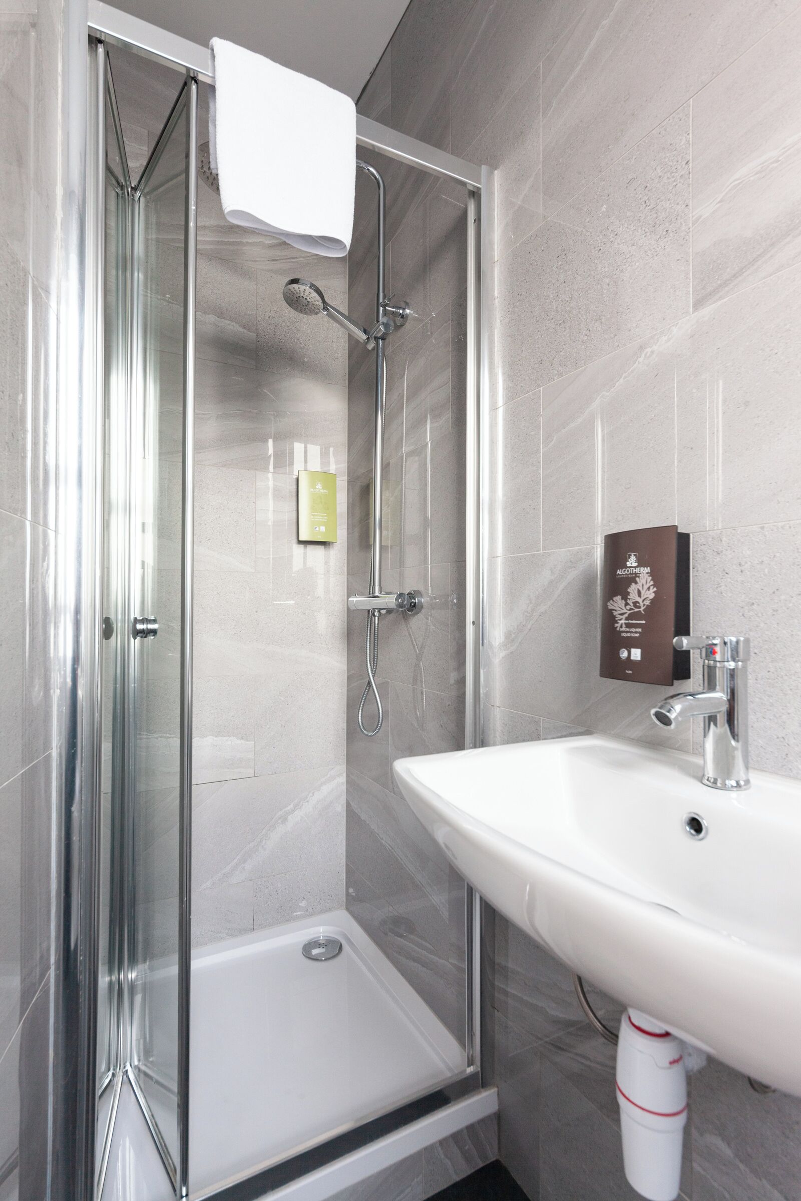 A modern bathroom with a glass-enclosed shower, a white sink, and a soap dispenser.