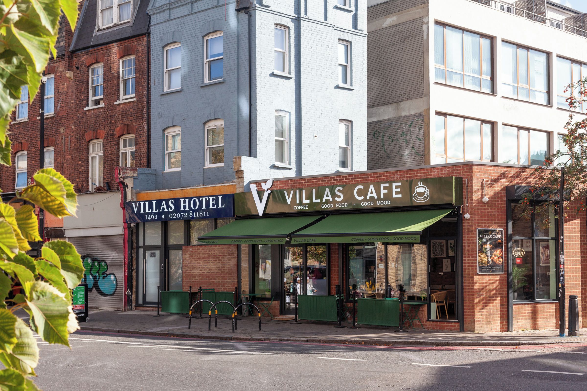 A street view of a hotel and a cafe with a green awning, a visible entrance, and a clear sky.