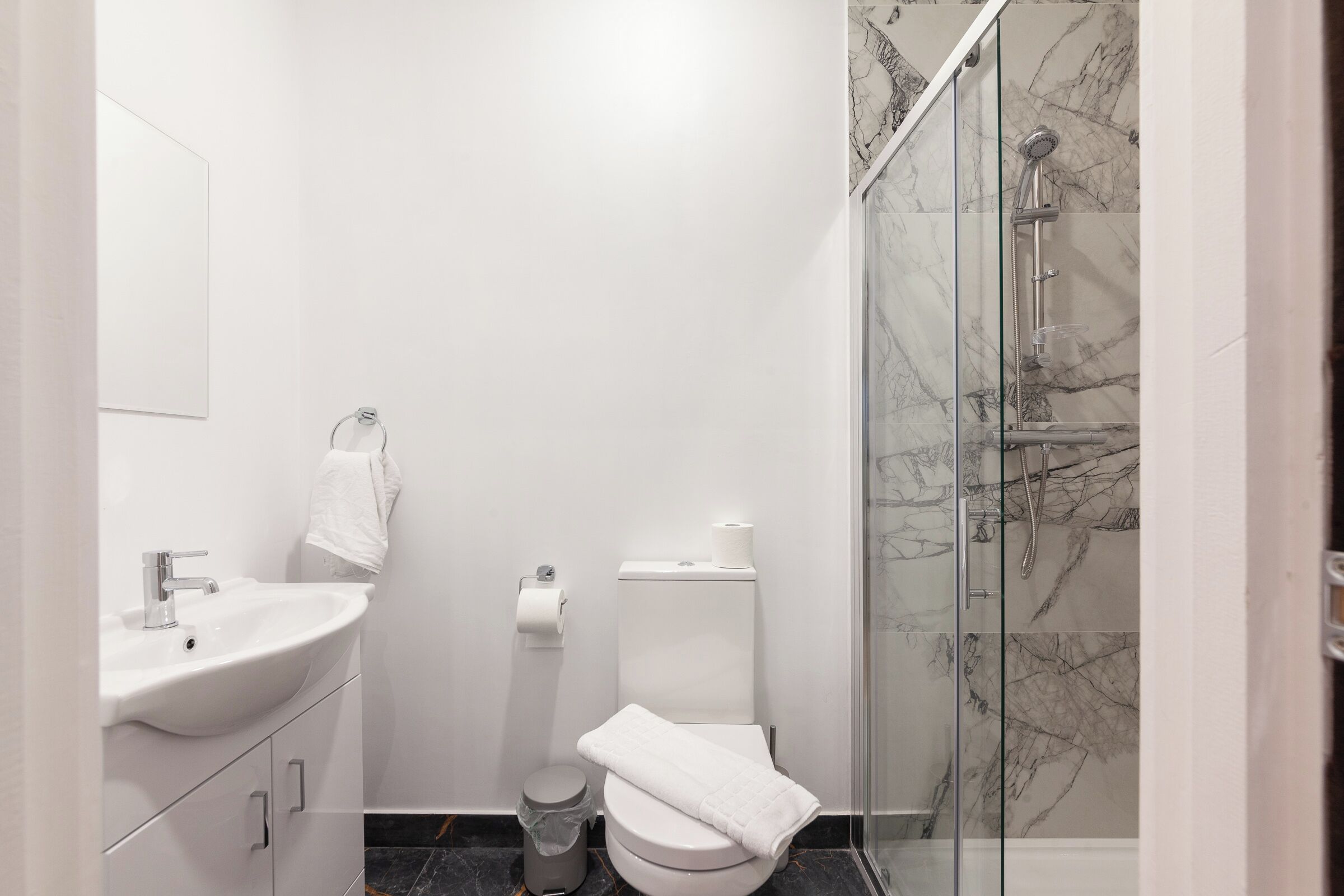 A modern bathroom with a white sink, toilet, and glass-enclosed shower.
