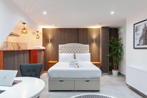 A modern hotel room with a large bed, bedside tables, a desk, and a potted plant. - Villas Apart Hotel (London)