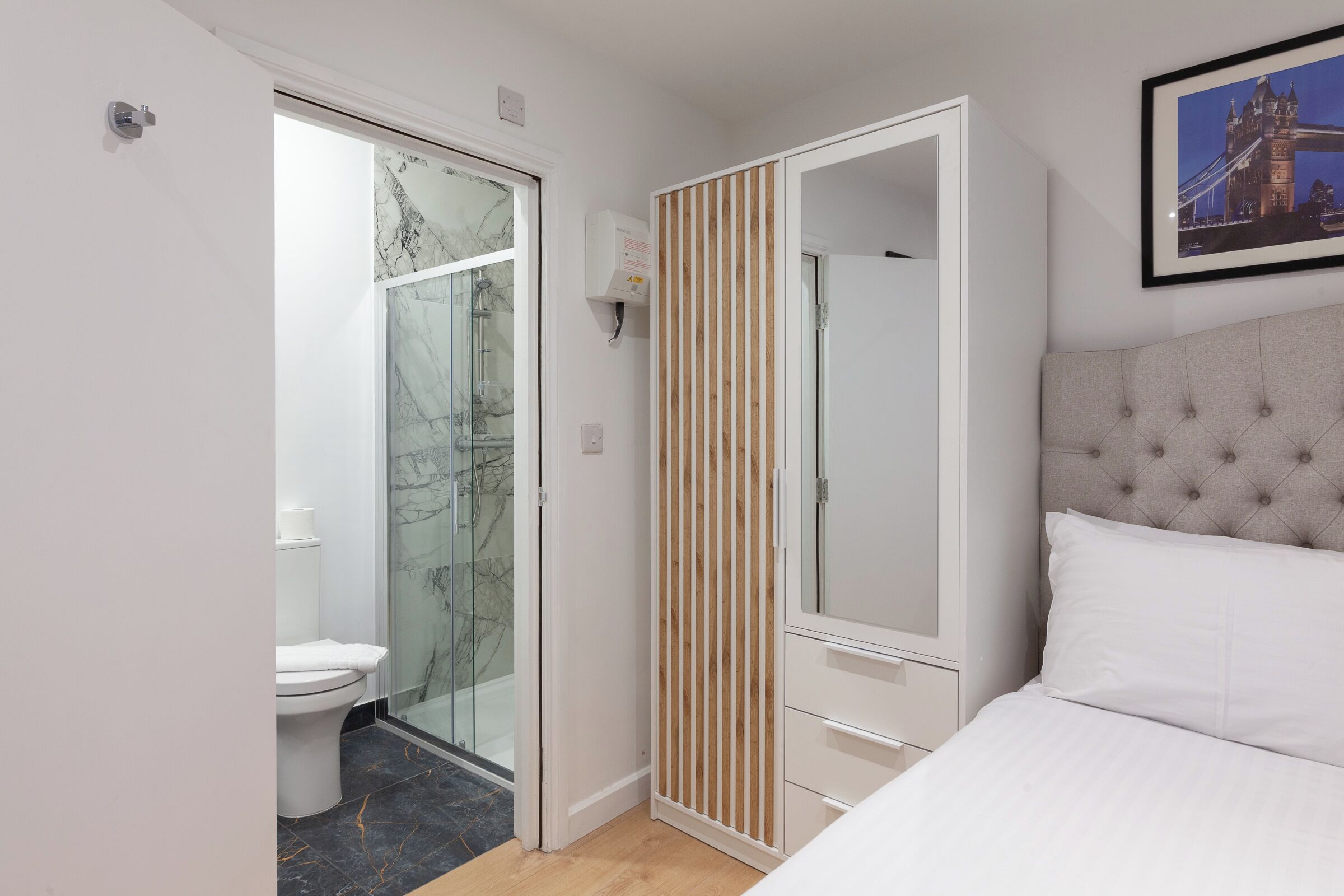 A bedroom with a bed, a wardrobe, and a bathroom with a toilet and shower.