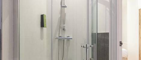 Una ducha con cerramiento de vidrio, un lavamanos blanco y una toalla colgada en la puerta.